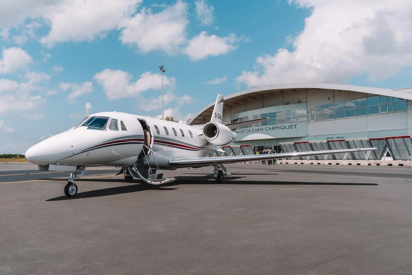 Jet privé sur le tarmac devant la façade vitrée et la toiture courbée du terminal de l'aéroport de Caen-Carpiquet.
