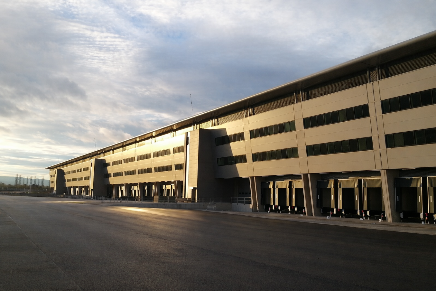 Façade monumentale de l'aérogare logistique Bâle-Mulhouse baignée de lumière, mettant en valeur la grande échelle de cet équipement de fret.